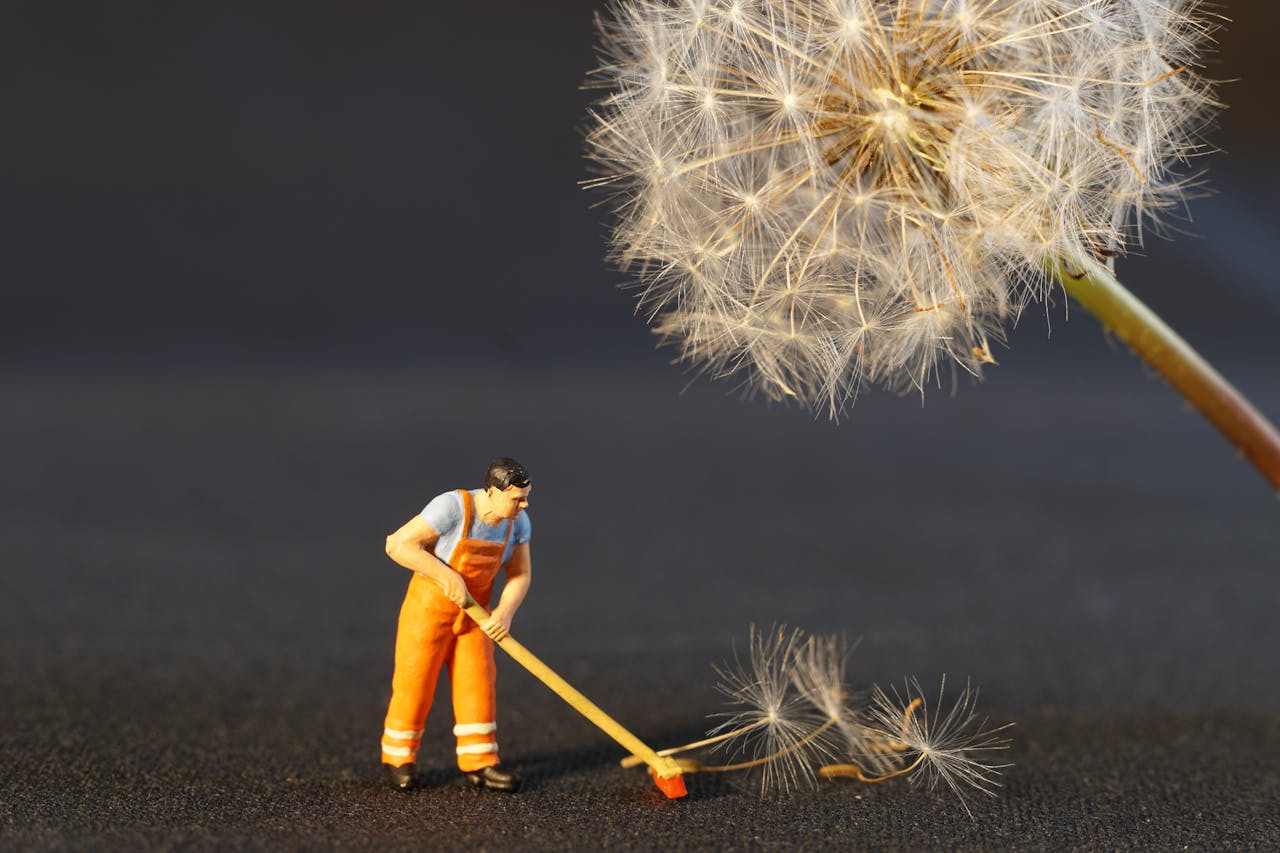 Close-up of a miniature worker figurine cleaning dandelion seeds, combining nature and toy elements.